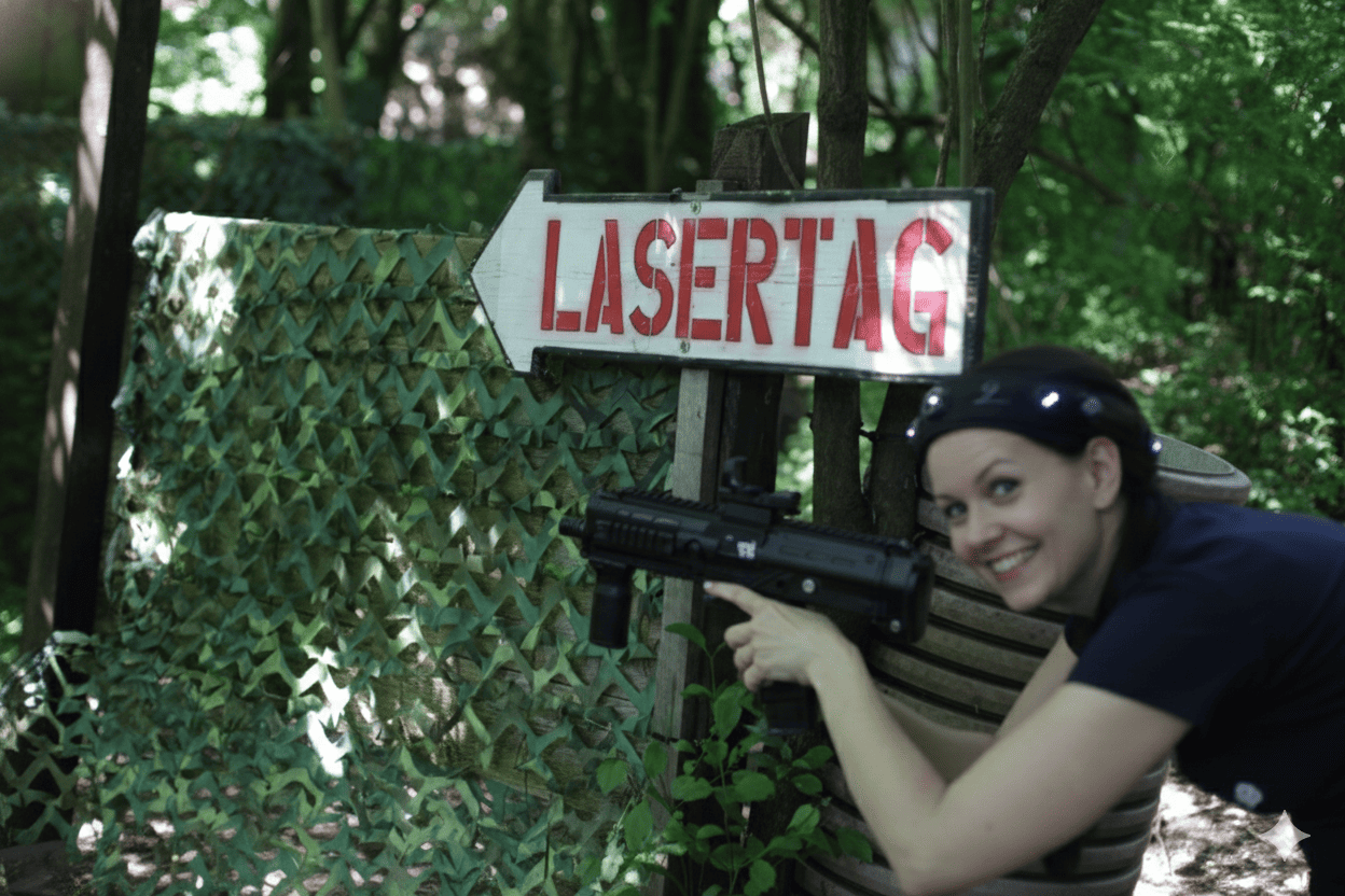 Outdoor Lasertag Wels Action Erlebnis: Lächelnde Spielerin mit Lasertag in der Nähe Markierer im Dschungel-Spielfeld. Wegweiser Lasertag