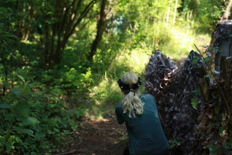 Lasertag Taktik und Deckung im Dschungel pielerin von hinten beim Outdoor Lasertag Wels, in geduckter Haltung zwischen Tarnnetzen und Büschen im Dschungel Spielfeld Marchtrenk. Fokus auf Taktik und Verbergen.